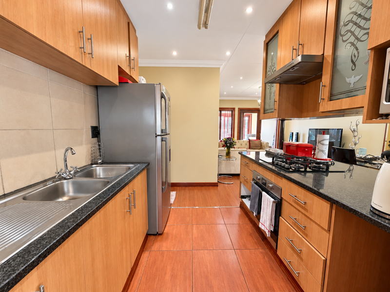A functional kitchen featuring wooden cabinetry, granite countertops, a gas hob, built-in oven, and stainless steel double sink with tiled flooring.