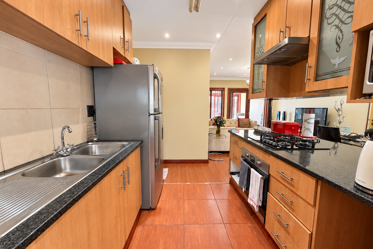 A functional kitchen featuring wooden cabinetry, granite countertops, a gas hob, built-in oven, and stainless steel double sink with tiled flooring.