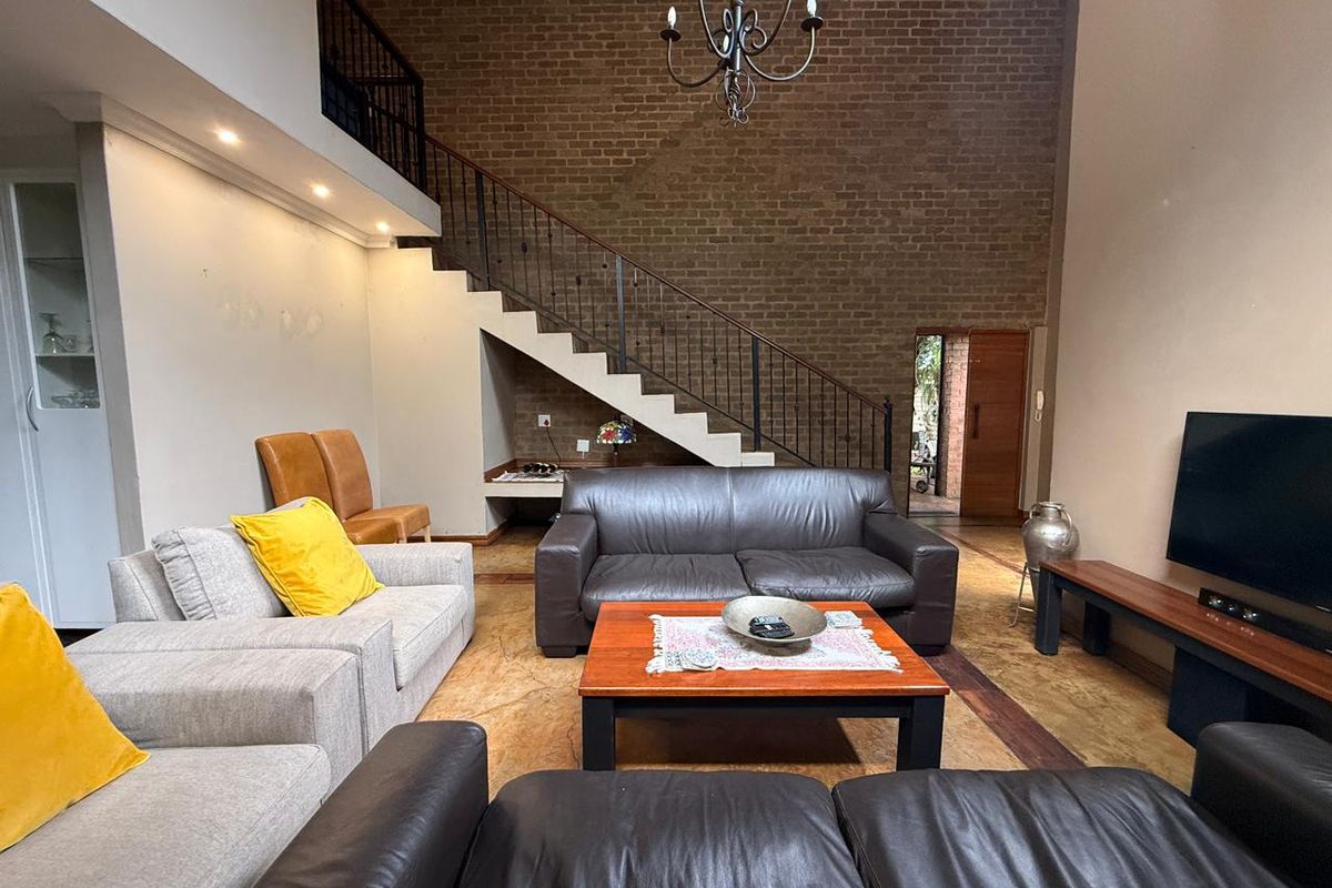 Spacious double-volume living area featuring an exposed brick feature wall, a staircase with wrought iron balustrades, and polished concrete flooring.