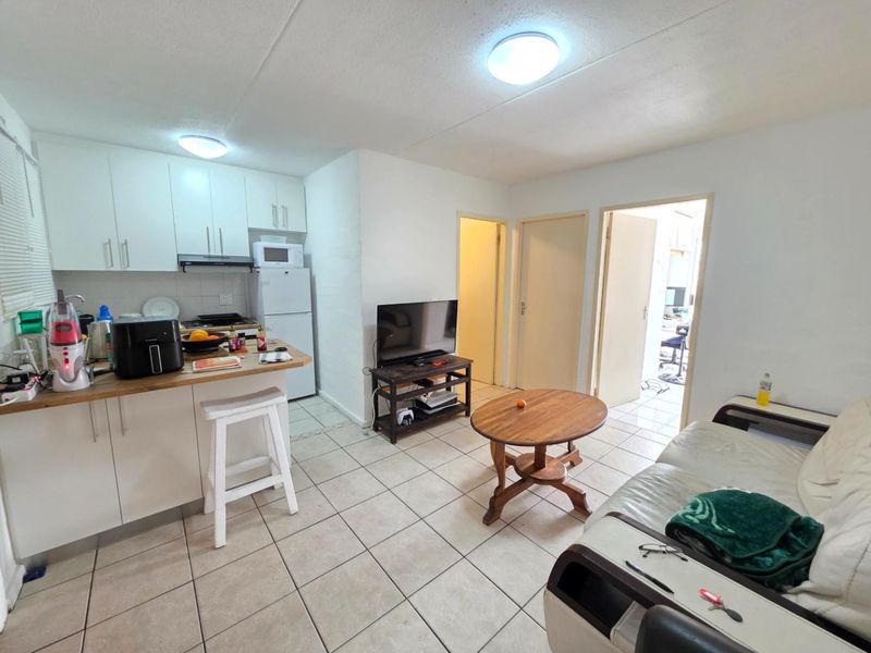 Open-plan living area featuring a compact kitchen with white cabinetry and tiled flooring, providing a functional layout for modern apartment living.