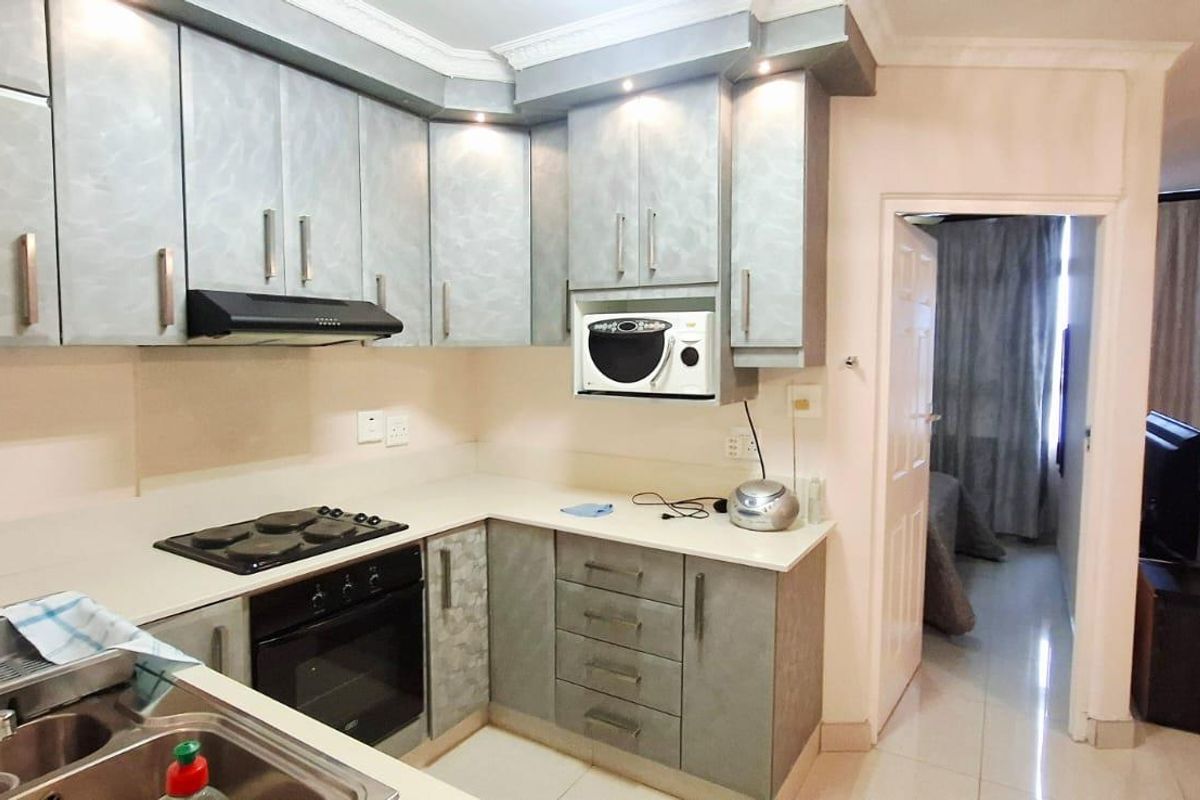 Compact kitchen featuring built-in cabinetry, integrated oven, hob, and extractor fan, with an open-plan layout flowing into the adjacent living area.