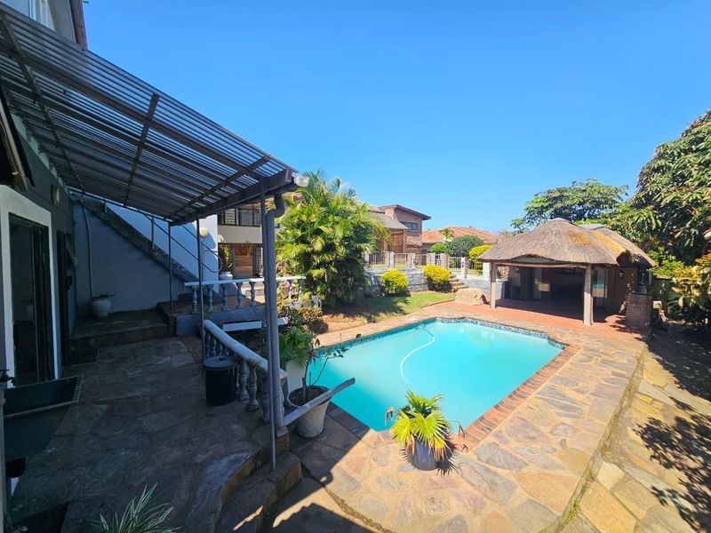 Outdoor pool area featuring a swimming pool, stone paving, and a thatched lapa, providing a functional space for outdoor entertainment.