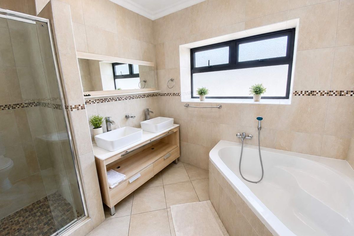 Modern bathroom featuring a double vanity with vessel sinks, a separate glass-enclosed shower, and a built-in bathtub with neutral tiled finishes.