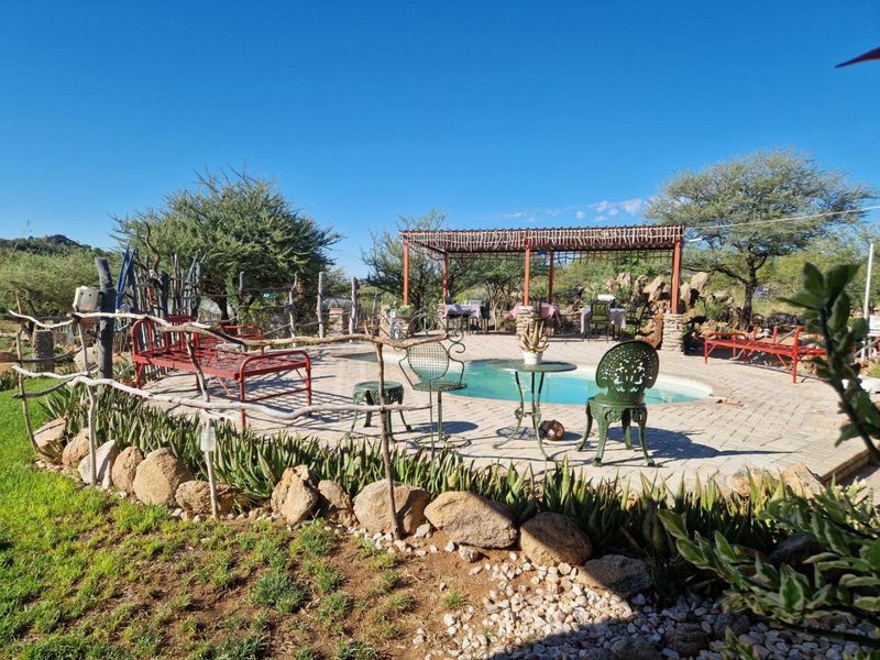 Outdoor pool area featuring a paved deck, a rustic pergola structure, and natural stone landscaping elements in a lodge setting.