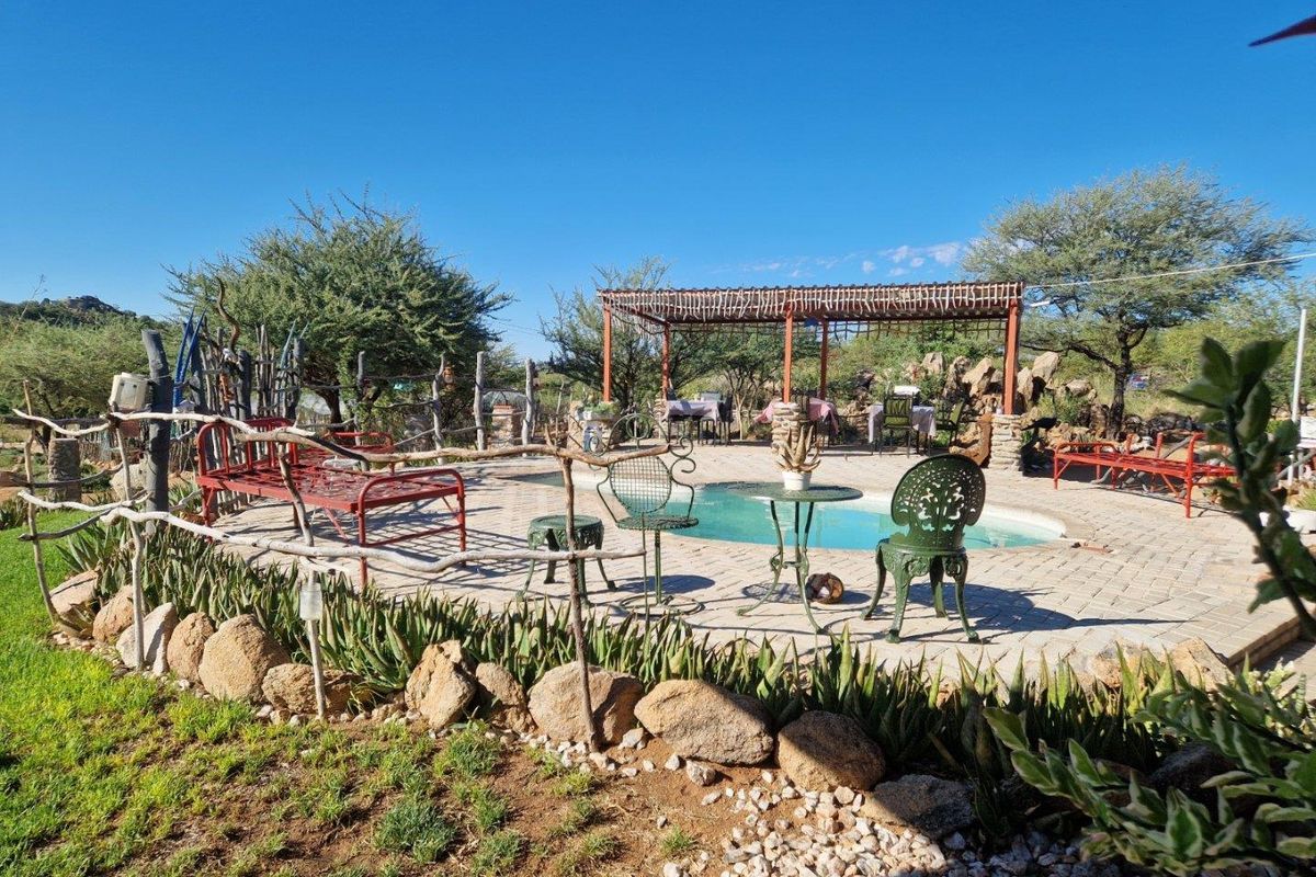 Outdoor pool area featuring a paved deck, a rustic pergola structure, and natural stone landscaping elements in a lodge setting.