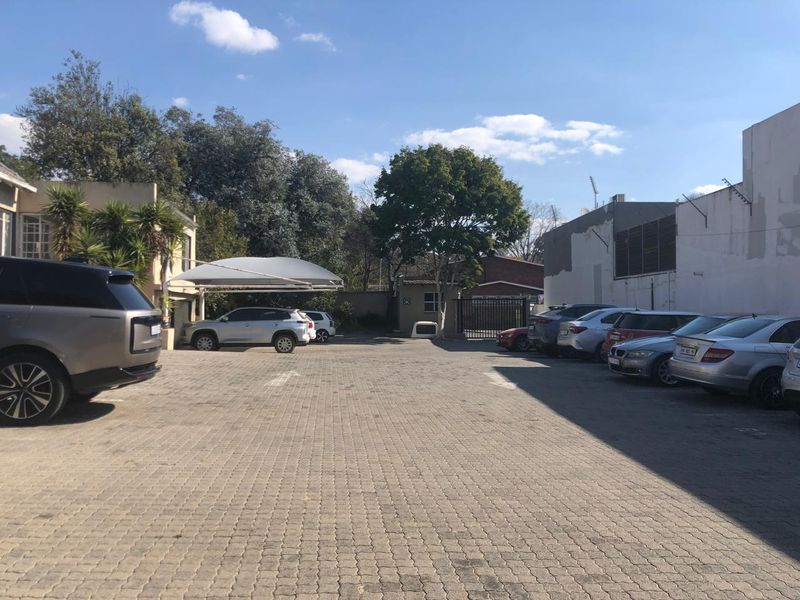 Exterior view of the office property featuring a paved parking area, shade port, and secure gated access.