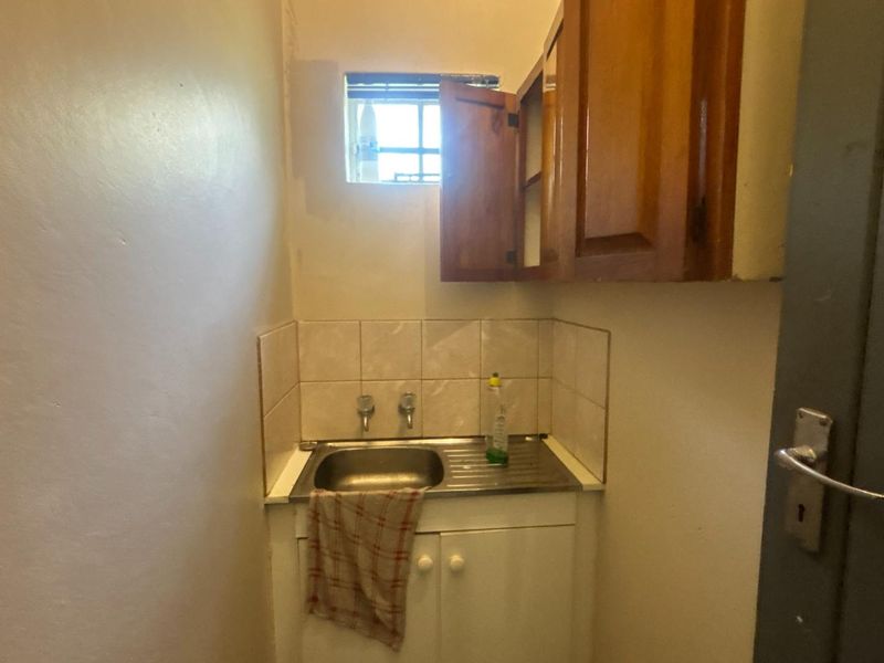 A compact scullery area featuring a stainless steel sink, tiled splashback, and built-in wooden cabinetry, providing functional utility space.