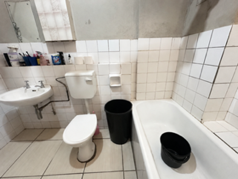 A dated bathroom featuring a bathtub, wall-mounted basin, and toilet, requiring significant renovation and finishing of wall surfaces.