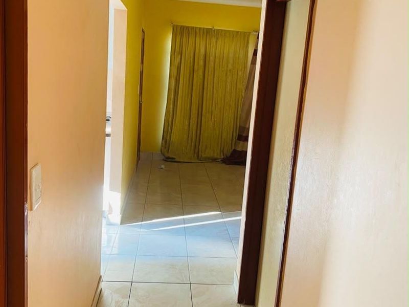 A simple interior hallway featuring tiled flooring and connecting to adjacent rooms, showing signs of wear and requiring cosmetic updates.
