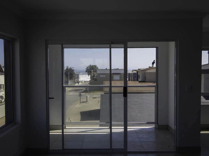 An empty living area featuring tiled flooring and large sliding glass doors that open onto a balcony with coastal views.