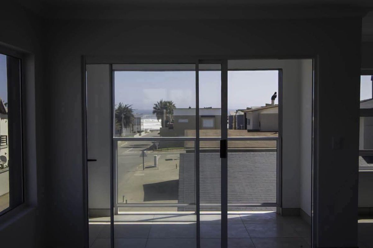 An empty living area featuring tiled flooring and large sliding glass doors that open onto a balcony with coastal views.