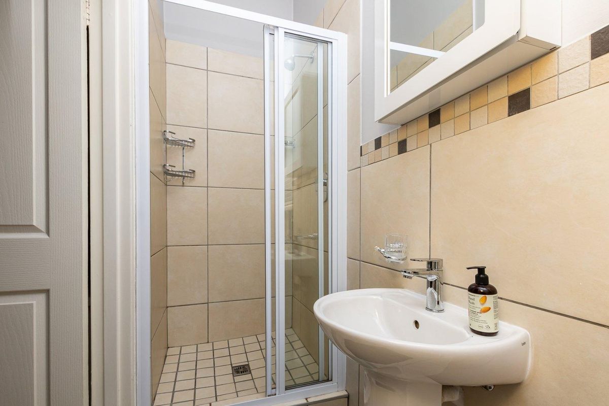 Compact bathroom featuring a tiled shower enclosure with glass door, pedestal basin, and wall-mounted mirror cabinet.