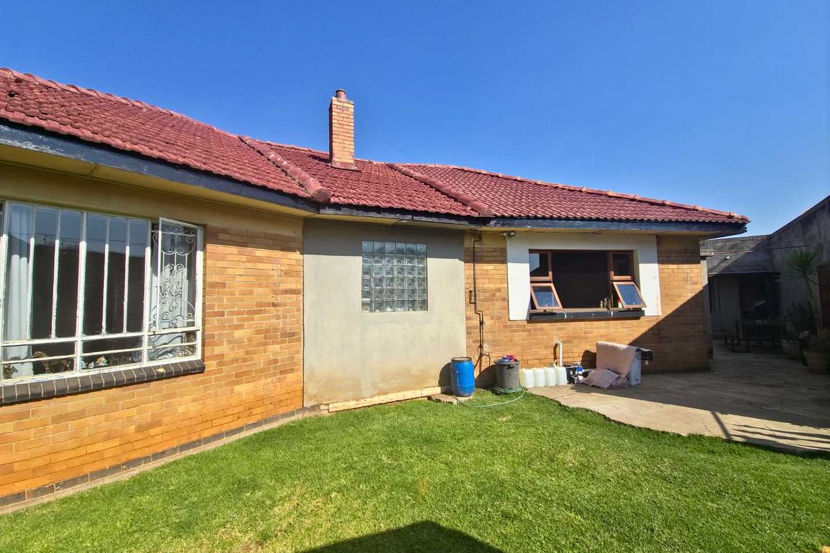 Rear view of the house featuring a brick facade, tiled roof, glass block window, and a small paved patio area leading to the garden.