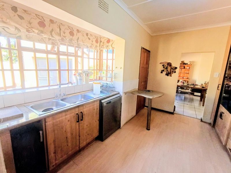 A functional kitchen featuring wooden cabinetry, a double stainless steel sink, stone countertops, and a built-in breakfast bar with access to the dining area.
