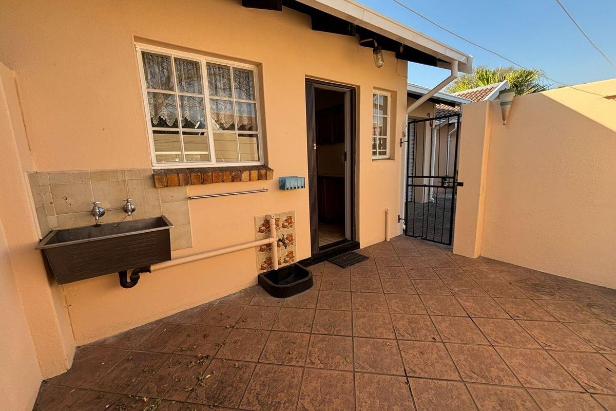 A paved rear patio area featuring a built-in utility sink, security gate, and direct access to the interior of the retirement unit.