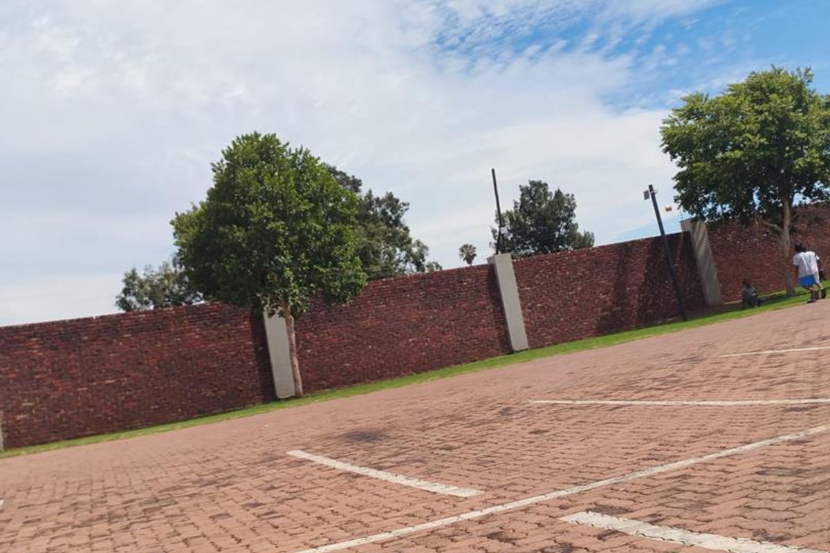 An outdoor parking area featuring paved ground with marked bays and a perimeter brick boundary wall with concrete pillars.