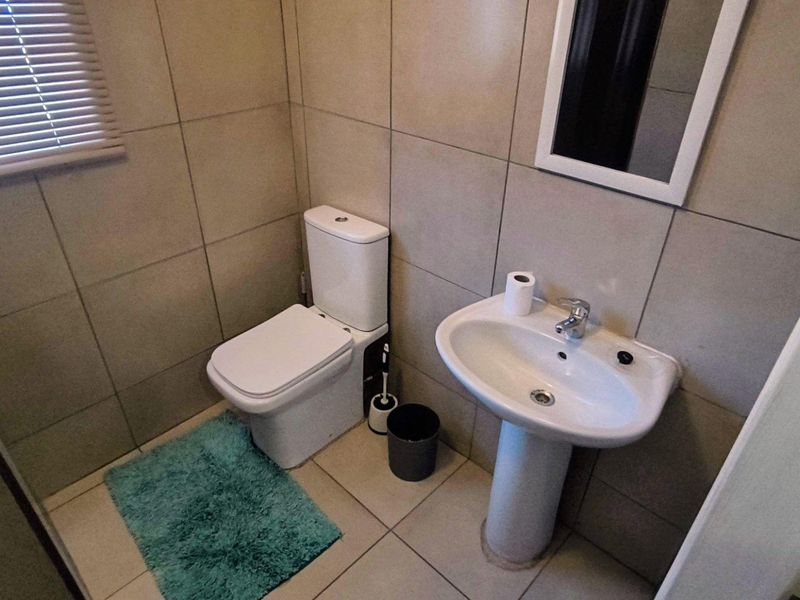 A compact guest bathroom featuring neutral wall and floor tiles, a white pedestal basin, and a standard toilet.