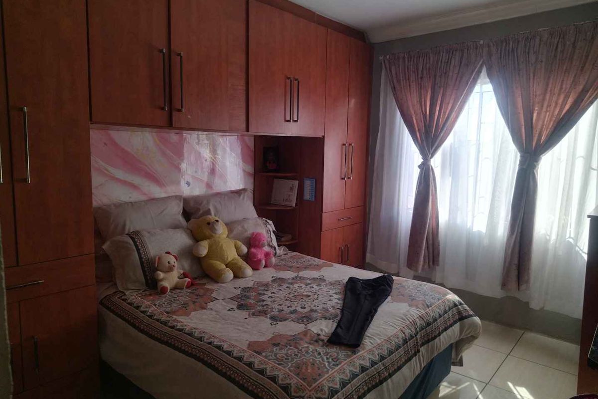 A bedroom featuring extensive built-in wooden cabinetry, tiled flooring, and a window fitted with security bars.