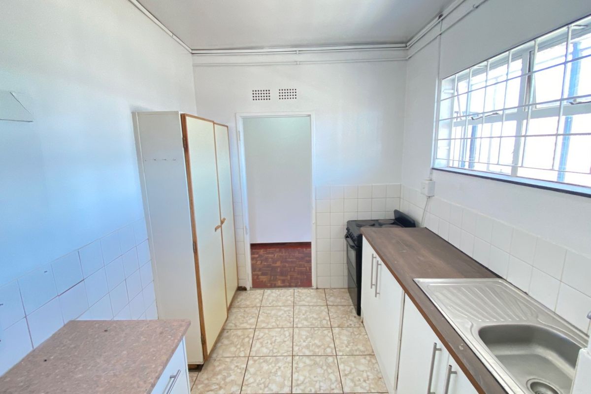 A functional kitchen featuring tiled flooring, built-in cabinetry, a stainless steel sink, and a tiled backsplash with security bars on the window.