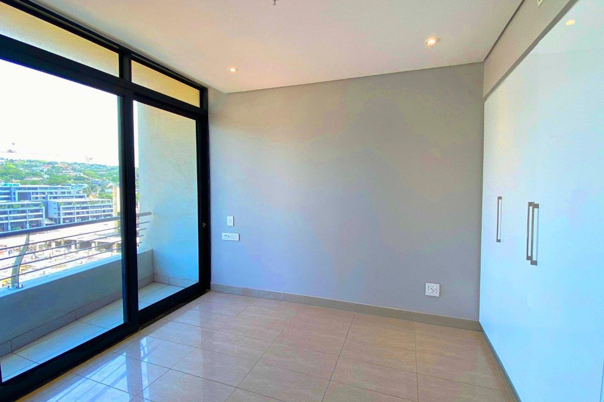 A bright, empty bedroom featuring modern tiled flooring, built-in cupboards, and a large sliding glass door providing access to a balcony with city views.