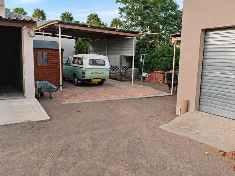Rear exterior area featuring a paved carport, a garage with a metal roller door, and an open driveway space.