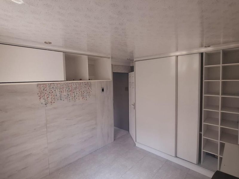 A clean, empty bedroom featuring extensive built-in white cabinetry, shelving, recessed ceiling lighting, and neutral tiled flooring.