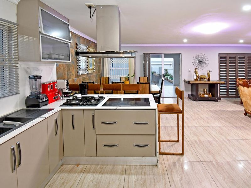 Open-plan kitchen and living area featuring modern cabinetry, dual cooktops, stone-look wall cladding, and large format floor tiles leading to an outdoor patio.