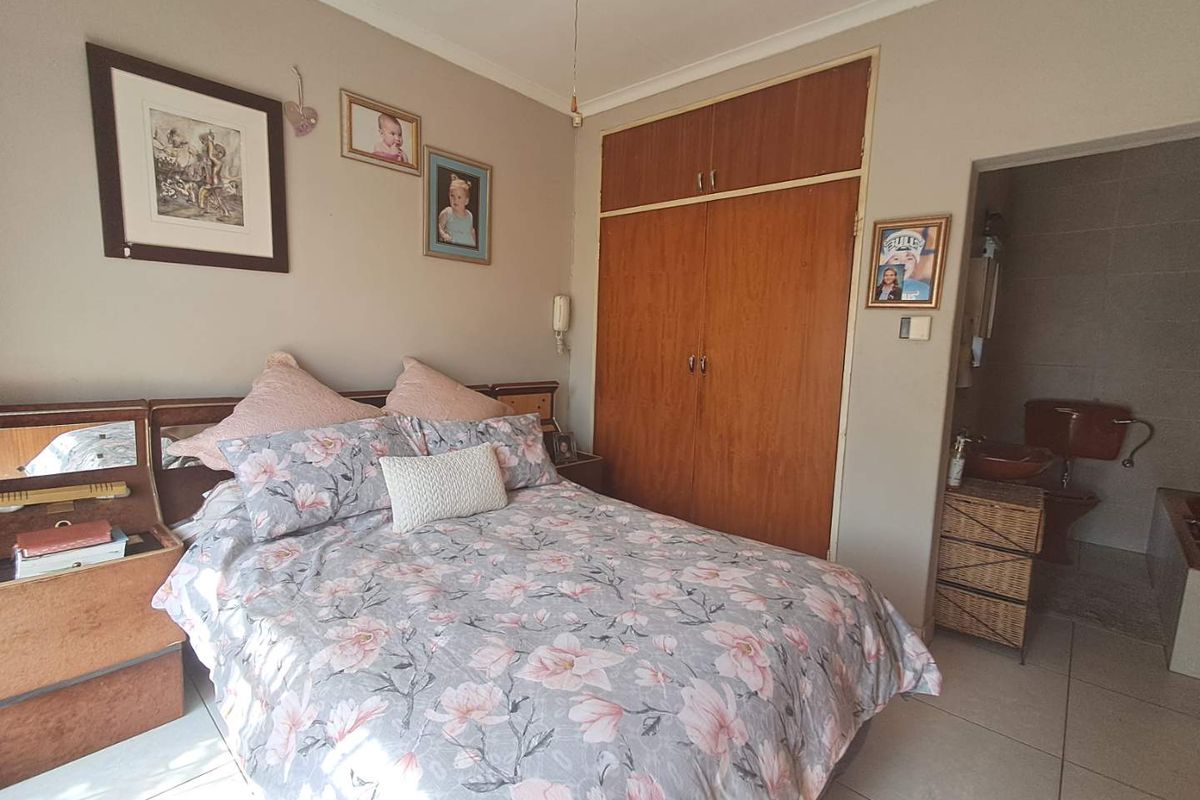 A bedroom featuring built-in wooden cupboards and an en-suite bathroom, finished with neutral wall tones and tiled flooring.