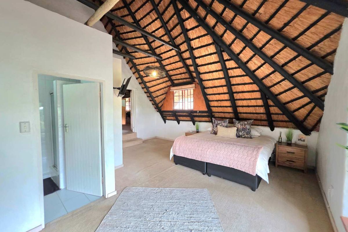 Spacious bedroom featuring a high vaulted thatched roof with exposed timber beams, carpeted flooring, and an en-suite bathroom entrance.