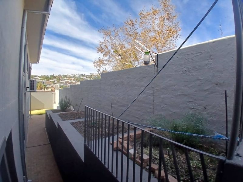 A side exterior view featuring a paved walkway, raised garden beds with metal railings, and a painted masonry retaining wall.