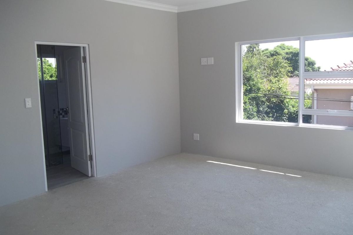 A bright, empty bedroom featuring neutral grey walls, crown molding, and an en-suite bathroom entrance, offering a clean canvas for personalization.
