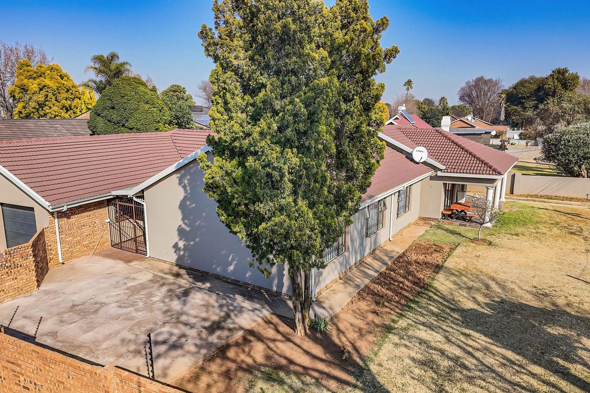 Aerial view of a residential property featuring a tiled roof, concrete driveway, garage, and a spacious garden with perimeter wall and electric fencing.