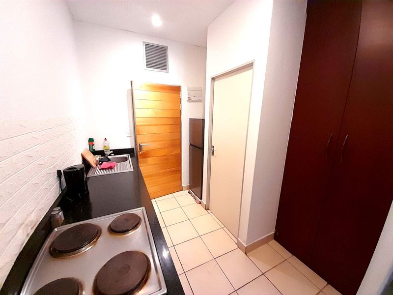 Compact kitchen featuring a built-in electric hob, stainless steel sink, tiled flooring, and ample built-in storage cabinetry.