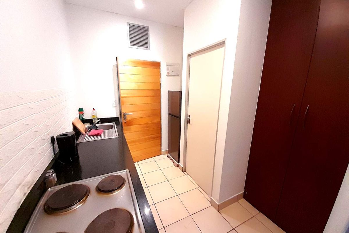 Compact kitchen featuring a built-in electric hob, stainless steel sink, tiled flooring, and ample built-in storage cabinetry.