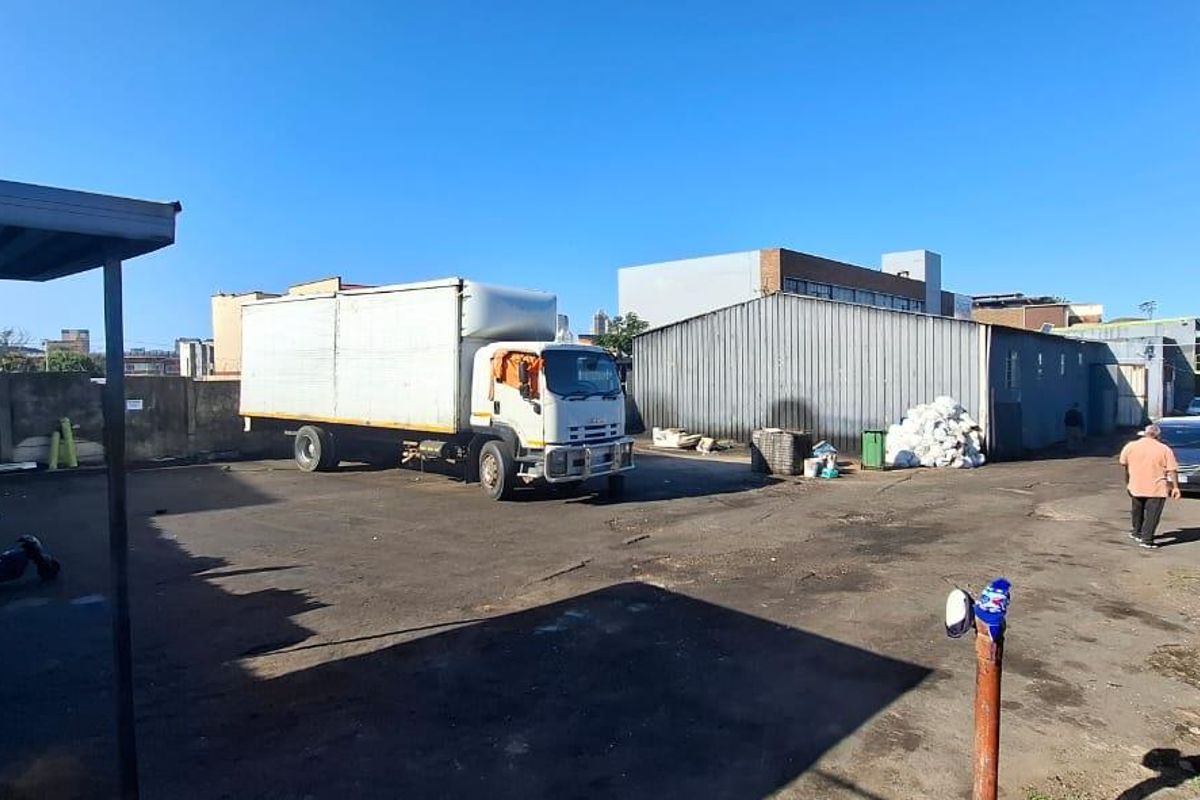 A paved industrial yard featuring a metal-clad warehouse structure, perimeter boundary walls, and a covered loading area suitable for commercial logistics.