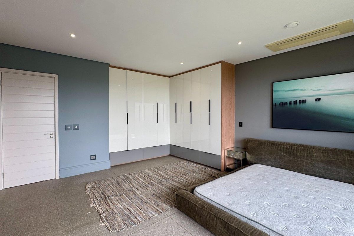 Modern bedroom featuring extensive built-in high-gloss cabinetry, recessed lighting, and integrated ducted air conditioning, finished with neutral tiled flooring.