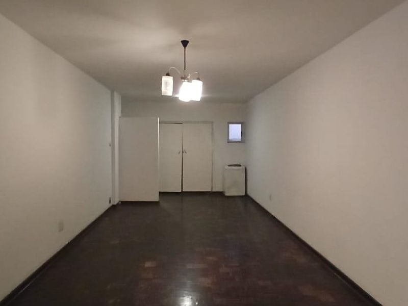 An empty, rectangular living area featuring dark parquet flooring, built-in storage cupboards, and a central ceiling light fixture.