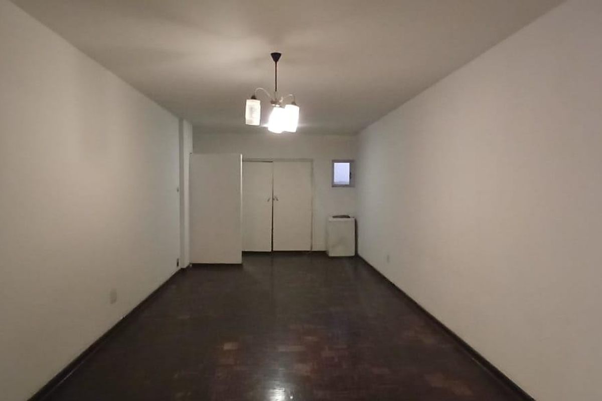 An empty, rectangular living area featuring dark parquet flooring, built-in storage cupboards, and a central ceiling light fixture.