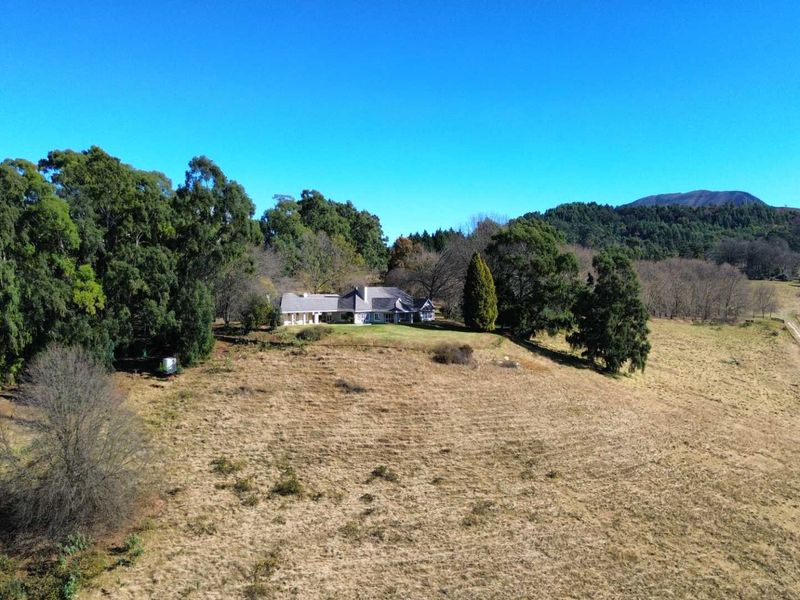 An aerial view of a farmhouse situated on a large rural property with expansive fields, mature trees, and a dirt access road.