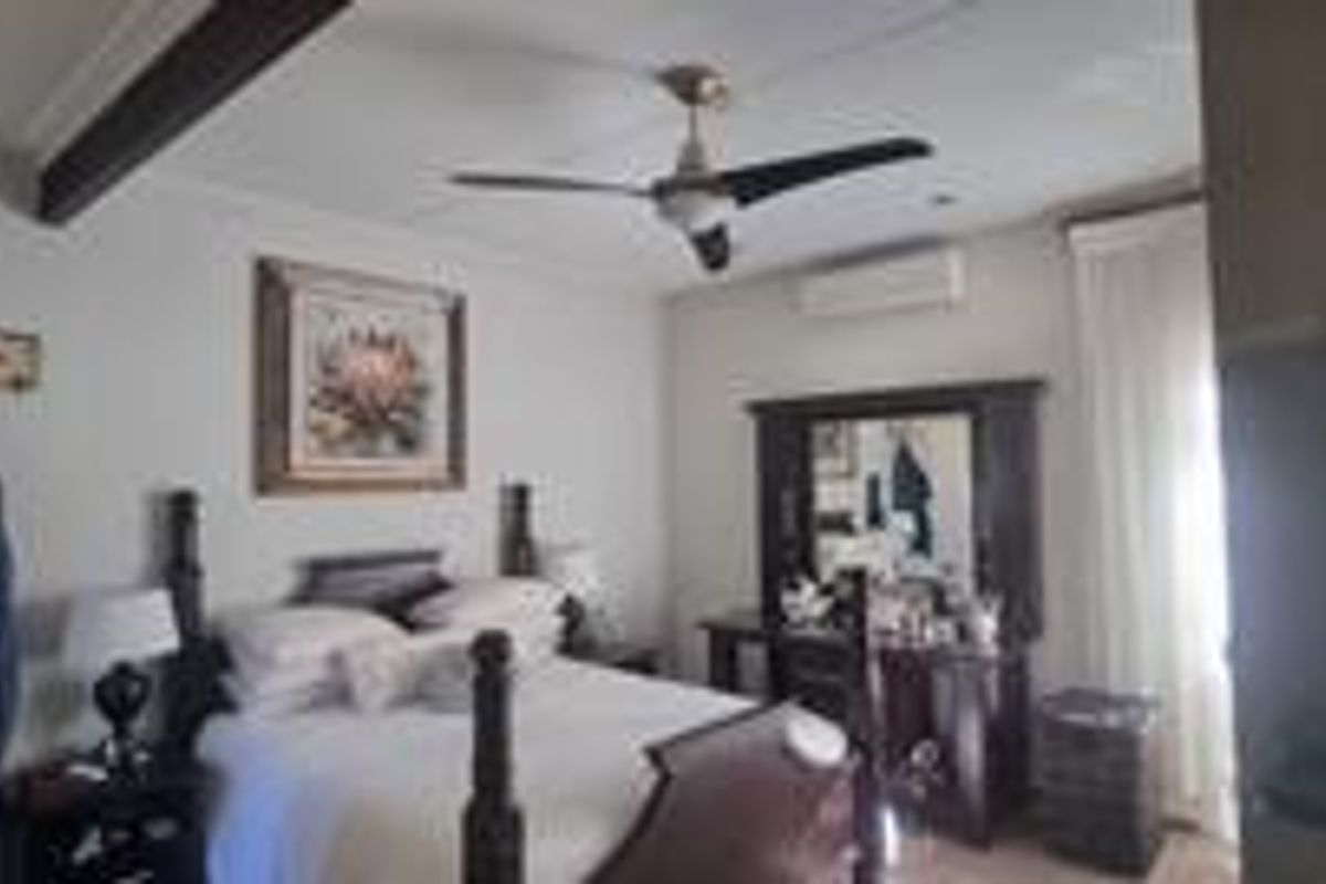A bedroom featuring an exposed ceiling beam, a ceiling fan, and a wall-mounted split-system air conditioner.