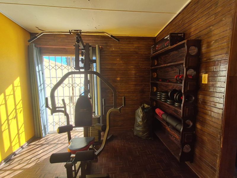 A home gym space featuring timber wall paneling, parquet flooring, and a sliding door with a security gate, showing signs of ceiling wear.