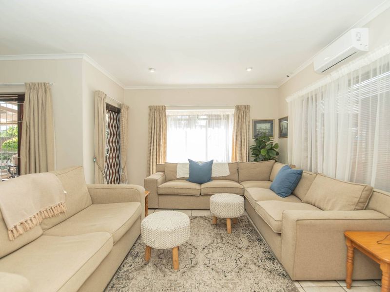 A bright and comfortable living room featuring tiled flooring, recessed downlighting, and a wall-mounted split-system air conditioner for climate control.