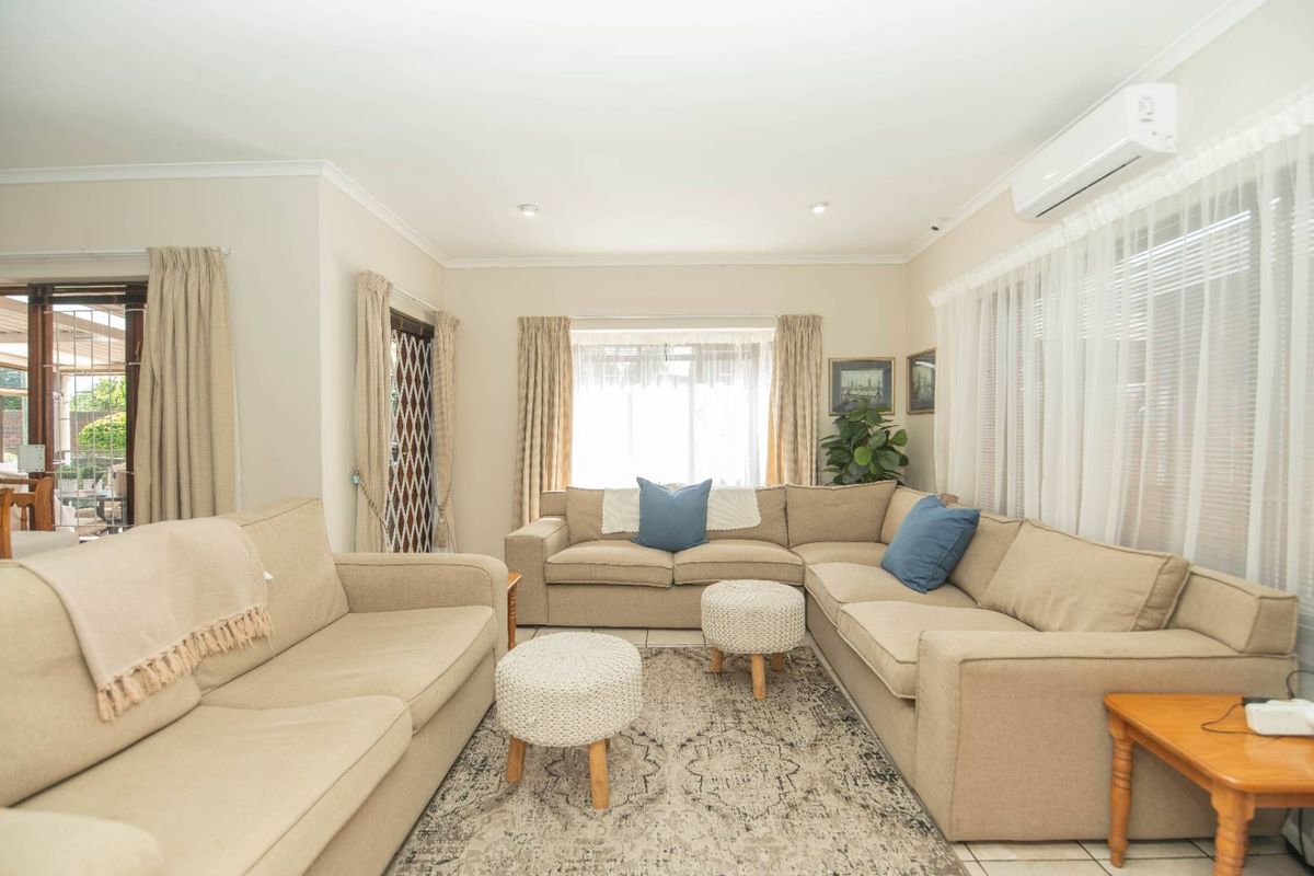 A bright and comfortable living room featuring tiled flooring, recessed downlighting, and a wall-mounted split-system air conditioner for climate control.