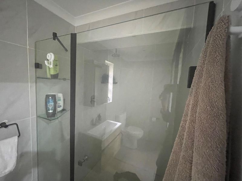 A modern bathroom featuring a glass-enclosed shower, wall-mounted vanity with basin, and toilet, finished with neutral wall and floor tiles.