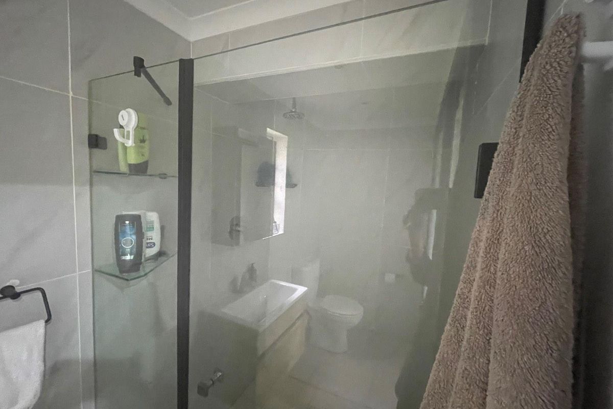 A modern bathroom featuring a glass-enclosed shower, wall-mounted vanity with basin, and toilet, finished with neutral wall and floor tiles.