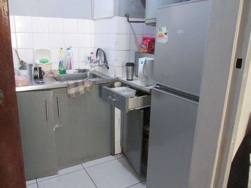 A compact kitchen area featuring built-in cabinetry, a stainless steel sink, and tiled backsplash, currently showing signs of wear and dated finishes.