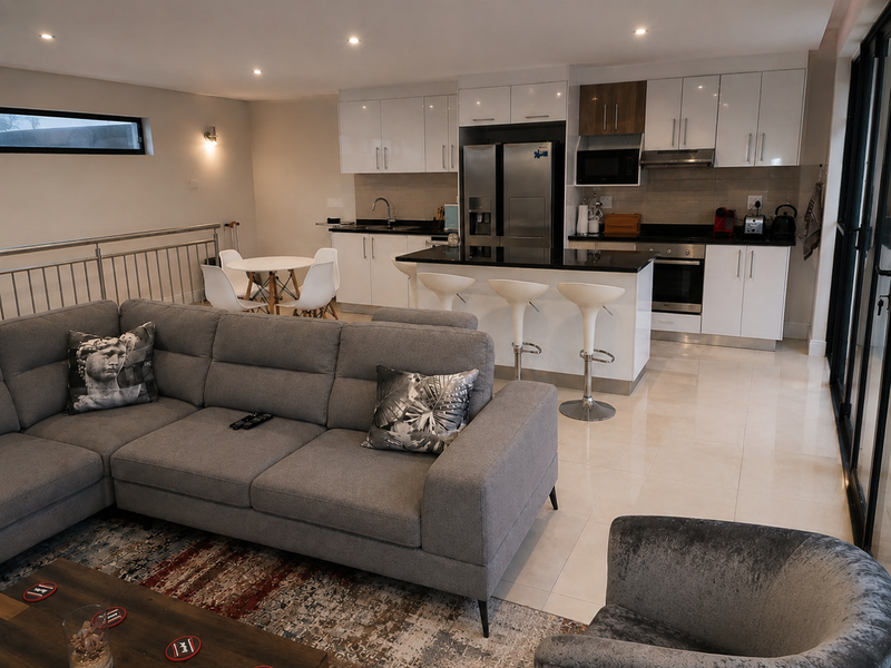Modern open-plan living area featuring a sleek kitchen with high-gloss cabinetry, stone countertops, a central island, and integrated appliances, flowing into a comfortable lounge space.