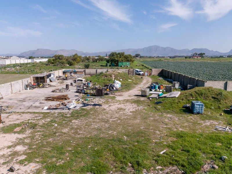 Aerial view of a vacant residential plot featuring a perimeter concrete wall, concrete slab area, and surrounding agricultural landscape.