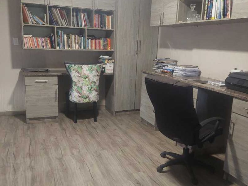 A functional home office featuring extensive built-in cabinetry, integrated desk space, and durable laminate flooring, providing ample storage and workspace.