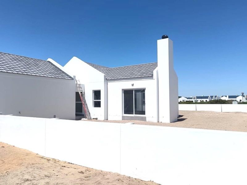 Rear view of a modern white house featuring a chimney, tiled roof, and sliding glass doors, set within a walled property with unfinished landscaping.